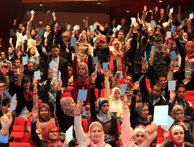 NDI Debate-Audience hold up cards to vote for the debate team from Yarmouk University, winner of Jordan&#039;s first-ever national student debate competition_Debating on allowing parties to operate in universities.JPG